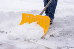 Person shoveling snow in driveway during winter snowstorm.